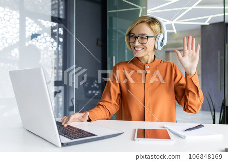 Young joyful woman at workplace listens to music in headphones, businesswoman dances and sings, sitting at work table inside office, female programmer well done successf technical project celebrates. 106848169