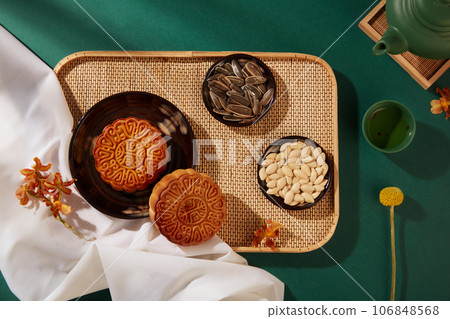 Bamboo tray with mooncakes and dishes of pumpkin seeds and sunflower seeds arranged on. Green background. Mid-Autumn Festival Food Advertising 106848568