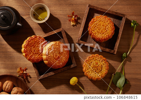 Baked mooncakes placed inside few wooden tray square-shaped. A dish of walnuts arranged. Beautiful various mooncakes prepared for mid autumn festival 106848615