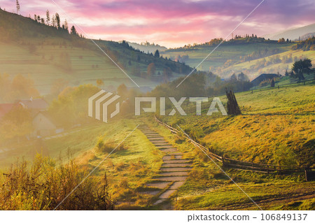 mountainous countryside on an autumn foggy weather at sunrise. empty rural fields on the hills. path to the village. mountain ridge in the distance beneath a sky with purple clouds 106849137