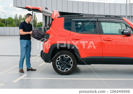 A man in a parking lot puts his suitcase in the trunk of a car. A man in a parking lot puts his suitcase in the trunk of a car. 106849998