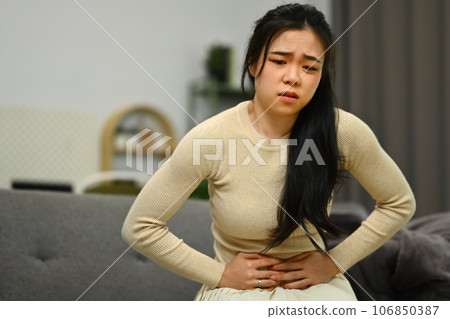 Young woman sitting on sofa at home suffering from stomachache, diarrhea or indigestive problem. Health care concept 106850387