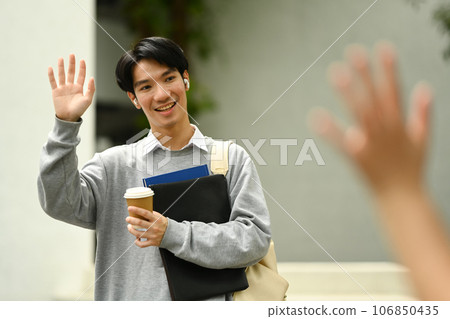 Smiling asian man waving hand and greeting hiss classmate. Education and youth lifestyle concept 106850435