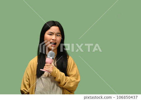Teenage girl singing songs with microphone, posing isolated on green background 106850437