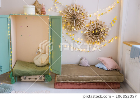The interior of a children's room decorated for the Christmas holidays. Soft mattresses with garlands in the form of stars and a children's wardrobe with soft pillows. 106852057
