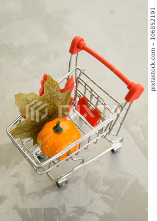 Grocery cart with decorative pumpkins and maple leaves on a concrete background. The concept of the autumn sales. Black Friday and cyber Monday. Grocery cart with decorative pumpkins and maple leaves on a concrete background. The concept of the autumn sales. Black Friday and cyber Monday. 106852191