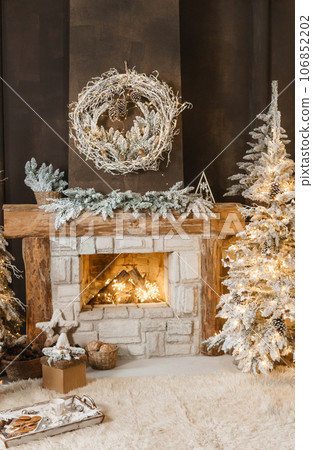 The interior of a room with a fireplace, Christmas trees with artificial snow and garlands, a blanket and a tray with hot drinks. The magical atmosphere of Christmas. The interior of a room with a fireplace, Christmas trees with artificial snow and garlands, a blanket and a tray with hot drinks. The magical atmosphere of Christmas. 106852202