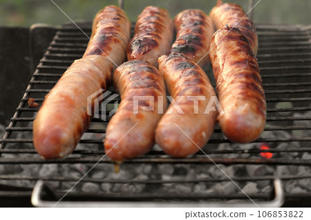 Grilled sausages. Cook man preparing grilling food bbq. Barbecue with smoke, flame outdoors. Tasty juicy german bratwurst. Charcoal kettle grill outside in backyard. Family summer vacation. Close-up Grilled sausages. Cook man preparing grilling food bbq. Barbecue with smoke, flame outdoors. Tasty juicy german bratwurst. Charcoal kettle grill outside in backyard. Family summer vacation. Close-up 106853822