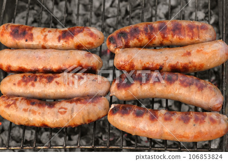 Grilled sausages. Cook man preparing grilling food bbq. Barbecue with smoke, flame outdoors. Tasty juicy german bratwurst. Charcoal kettle grill outside in backyard. Family summer vacation. Close-up Grilled sausages. Cook man preparing grilling food bbq. Barbecue with smoke, flame outdoors. Tasty juicy german bratwurst. Charcoal kettle grill outside in backyard. Family summer vacation. Close-up 106853824