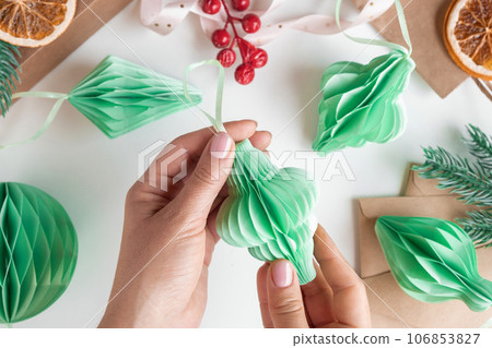 Female hands unfold paper Christmas honeycomb ornaments. Handmade foldable plastic free decor. Concept of winter creativity crafts. Trendy eco DIY. Scandinavian Modern decoration, minimalist. Top view 106853827