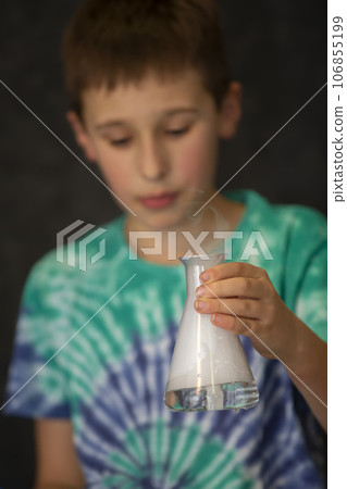 A boy conducts a scientific chemical experiment with liquid nitrogen. A child with a glass flask filled with smoke. A boy conducts a scientific chemical experiment with liquid nitrogen. A child with a glass flask filled with smoke. 106855199