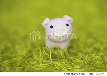 A pink piggy toy lies on the green carpet. There seems to be a piglet in the meadow. 106856474