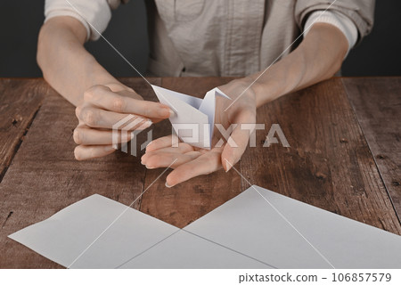 hands of an elderly woman fold origami paper. Creating an origami paper crane 106857579