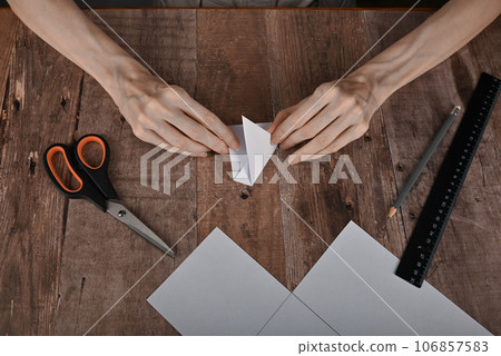 hands of an elderly woman fold origami paper. Creating an origami paper crane hands of an elderly woman fold origami paper. Creating an origami paper crane 106857583