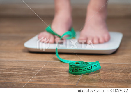 girl with swollen feet uses a scale next to a measuring tape on a wooden floor. Unrecognizable woman weighing herself 106857672