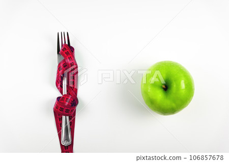 Green apple, fork and measuring tape. Diet concept. Diet for weight loss with a measuring tape and fruit on a white background, top view 106857678