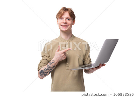 a young red-haired guy in glasses and a brown shirt holds a laptop in his hands. IT specialist 106858586