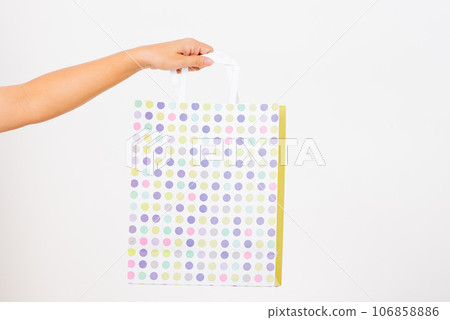 Closeup women hand holding a white circular pattern shopping bag, studio shot isolated on white background, female holds in hand white clear empty blank craft paper gift bag for purchases 106858886