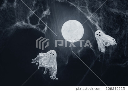 Ghosts of gauze on a dark background with a glowing moon and spiderwebs. Creative DIY Halloween decor. Halloween greeting card. Copy space. 106859215