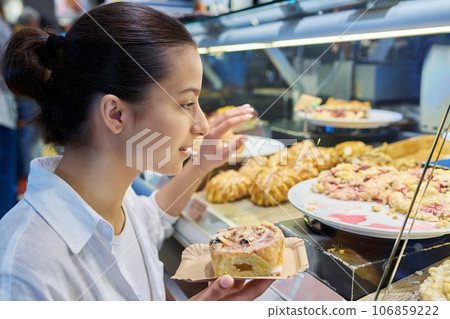 Young teenage female looking at sweet buns in glass display case in pastry shop Young teenage female looking at sweet buns in glass display case in pastry shop 106859222