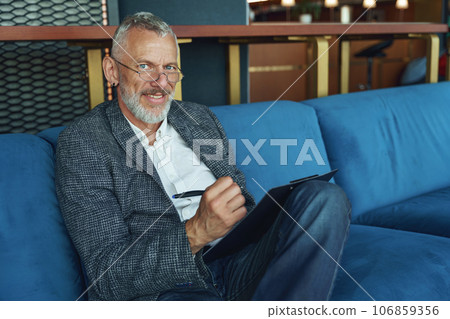 Senior executive manager is making notes in notepad while sitting sofa in cozy coworking 106859356