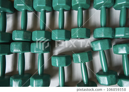 Close up of many green metal dumbbells lying on the floor at gym. Weight training equipment 106859358