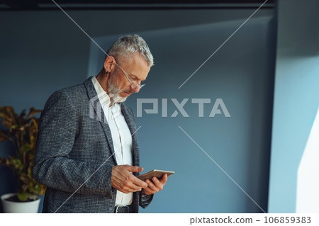 Focused mature businessman working on digital tablet while standing in office 106859383