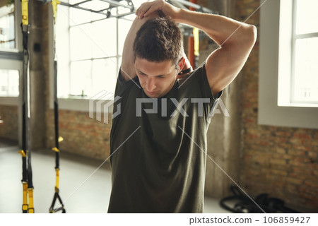 Close up of young sporty man in sportswear stretching his arm while standing at gym 106859427