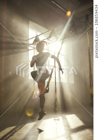 Professional training. Full-length of young athletic woman in sports clothing training legs with trx fitness straps in the gym. 106859434
