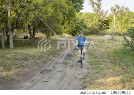 athletic senior man is riding a folding bike in Whitetail Campground in Nebraska National Forest athletic senior man is riding a folding bike in Whitetail Campground in Nebraska National Forest 106859651