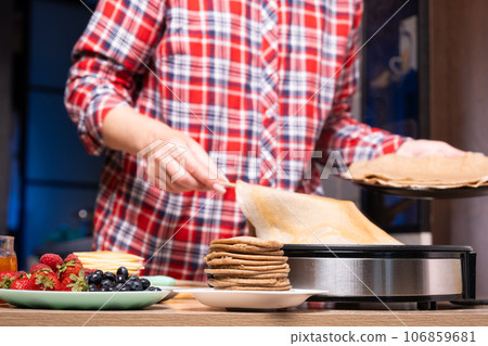 Woman cooking delicious crepe on electric pancake maker in kitchen, closeup 106859681