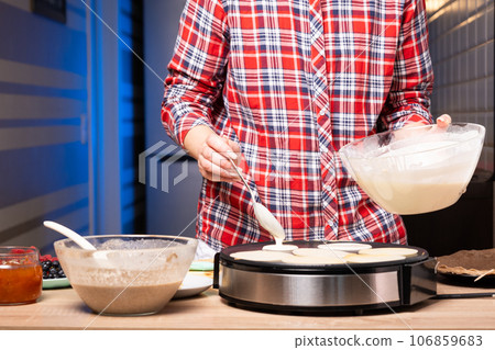 Woman cooking delicious crepe on electric pancake maker in kitchen, closeup 106859683