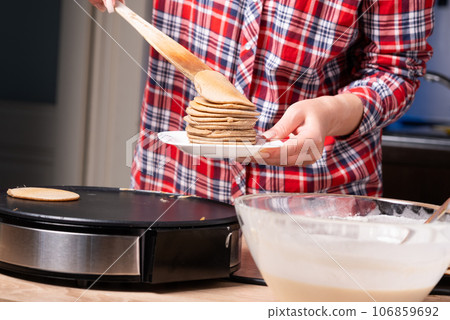 Woman cooking delicious crepe on electric pancake maker in kitchen, closeup 106859692