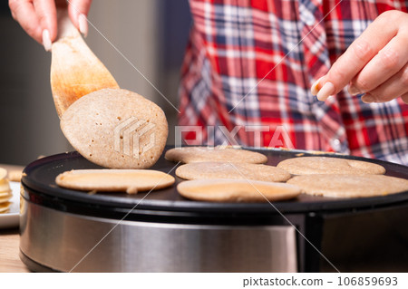 Woman cooking delicious crepe on electric pancake maker in kitchen, closeup Woman cooking delicious crepe on electric pancake maker in kitchen, closeup 106859693