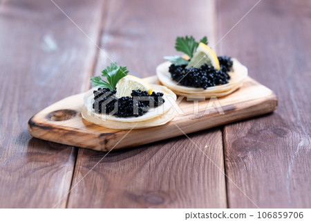 Appetizer, pancakes with black caviar and lemon on a wooden plate, close-up. 106859706