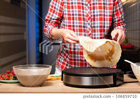 Woman cooking delicious crepe on electric pancake maker in kitchen, closeup Woman cooking delicious crepe on electric pancake maker in kitchen, closeup 106859710