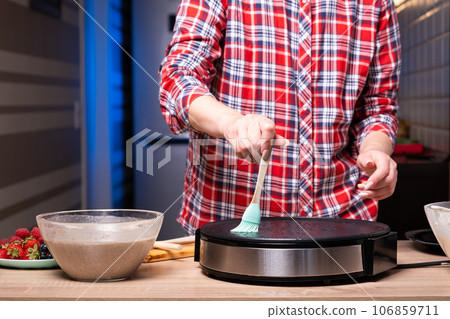 Woman cooking delicious crepe on electric pancake maker in kitchen, closeup 106859711