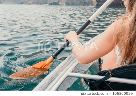 Woman in kayak back view. Happy young woman with long hair floating in transparent kayak on the crystal clear sea. Summer holiday vacation and cheerful female people relaxing having fun on the boat Woman in kayak back view. Happy young woman with long hair floating in transparent kayak on the crystal clear sea. Summer holiday vacation and cheerful female people relaxing having fun on the boat 106860039
