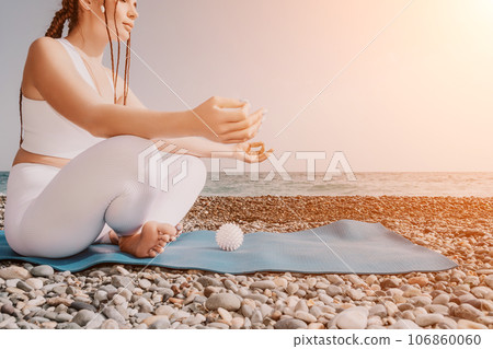 Close up Yoga Hand Gesture of Woman Doing an Outdoor meditation. Blurred sea background. Woman on yoga mat in beach meditation, mental health training or mind wellness by ocean, sea. Selective focus 106860060