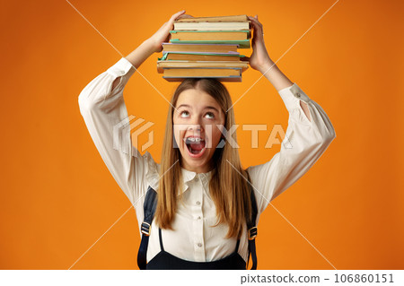 Teen schoolgirl holding stack of books over head on yellow background Teen schoolgirl holding stack of books over head on yellow background 106860151