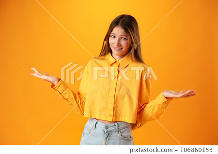Puzzled teen girl don't know what to do on yellow background in studio Puzzled teen girl don't know what to do on yellow background in studio 106860153