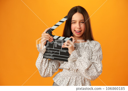 Happy smiling girl portrait holding clapper board on yellow background 106860185