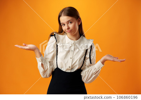 Teen girl shows I don't know gesture against yellow background Teen girl shows I don't know gesture against yellow background 106860196