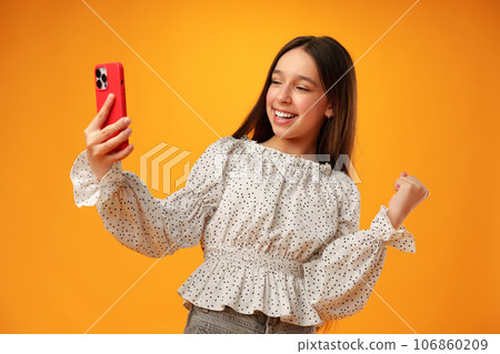 Surprised teen girl using mobile phone against yellow background Surprised teen girl using mobile phone against yellow background 106860209