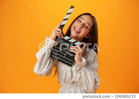 Happy smiling girl portrait holding clapper board on yellow background 106860235