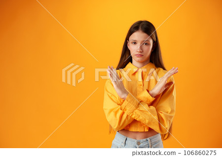 Teen girl shows cross hands gesture, rejecting something over yellow background in studio Teen girl shows cross hands gesture, rejecting something over yellow background in studio 106860275