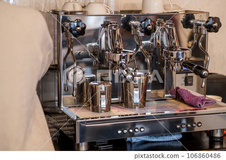 The barista prepares fresh coffee in the coffee machine in the morning in the cafe. There are coffee cups on the table for customers. Coffee machine close-up The barista prepares fresh coffee in the coffee machine in the morning in the cafe. There are coffee cups on the table for customers. Coffee machine close-up 106860486