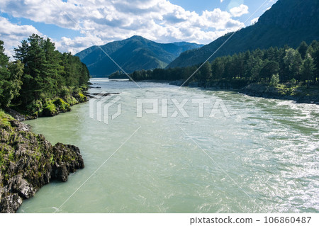 A wide, full-flowing mountain river with a fast current. Large stones stick out of the water. The large turquoise-colored mountain river Katun in the Altai Mountains, Altai Republic. A wide, full-flowing mountain river with a fast current. Large stones stick out of the water. The large turquoise-colored mountain river Katun in the Altai Mountains, Altai Republic. 106860487