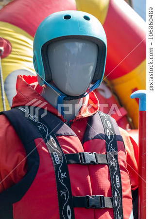 A mannequin in a red life jacket next to an inflatable boat as an advertisement for rafting or boating on the river in tourist places. A mannequin in a red life jacket next to an inflatable boat as an advertisement for rafting or boating on the river in tourist places. 106860489