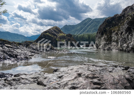 A wide, full-flowing mountain river with a fast current. Large stones stick out of the water. The large turquoise-colored mountain river Katun in the Altai Mountains, Altai Republic. A wide, full-flowing mountain river with a fast current. Large stones stick out of the water. The large turquoise-colored mountain river Katun in the Altai Mountains, Altai Republic. 106860560